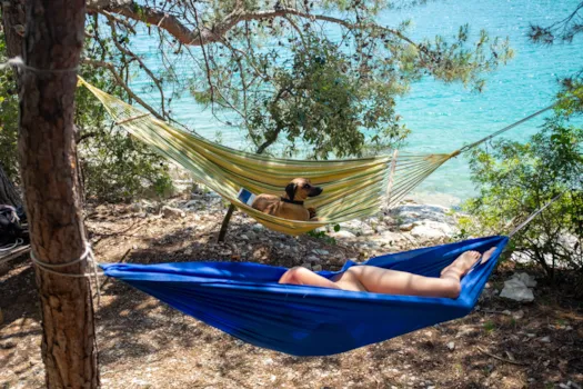Hund und nackte Frau entspannen in Hängematten am türkisblauen Meer.