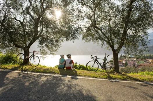 Paar mit Fahrrädern bei einer Pause, im Gras sitzend und blick auf den Gardasee