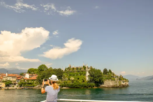 Junge Frau mit einem Panamahut, die im Sommer mit ihrem Smartphone die Isola Bella fotografiert, Lago Maggiore, Piemont, Italien