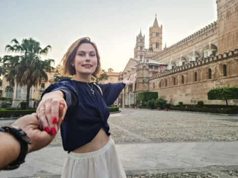 Eine Frau mittleren Alters vor der Kathedrale von Palermo auf Sizilien, die Hand ihres Partners haltend