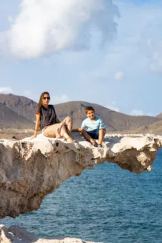 Mutter und Kind sitzen auf einem Felsen am Playa del Arco, Almería, Spanien