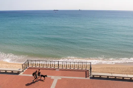 Zwei Touristen mit Hund am Balcó del Mediterrani in Tarragona mit Blick auf das Mittelmeer und Frachtschiffe am Horizont, Katalonien, Spanien
