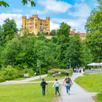 Blick auf einen Park mit Schloss Hohenschwangau im Hintergrund, mit Radfahrern und Fußgängern, Gastronomie für Touristen, Allgäu, Bayern, Deutschland