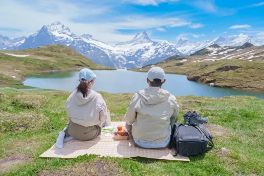 Ein Touristenpaar genießt ein Picknick am Bachalpsee mit Blick auf die verschneiten Schweizer Alpen am Grindelwald 