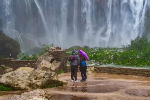 Ein Paar, das unter einem Regenschirm einen Wasserfall in Plitvice bewundert, Nationalpark Plitvicer Seen, Kroatien